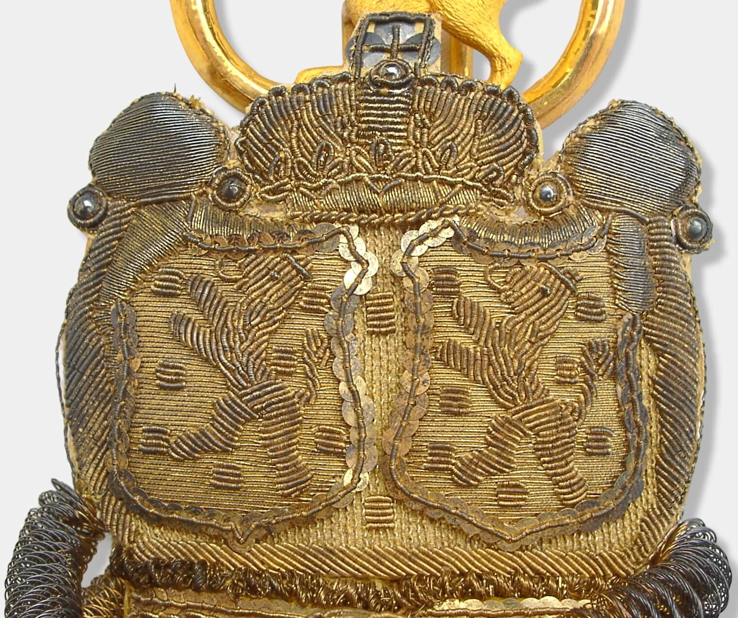 Teilansicht vom Portepee eines herzoglich nassauischen Kammerherrenschlüssels. Handstickereien aus vergoldeten Silberdrähten, im oberen Teil mit fünf (ursprünglich) vergoldeten Silberperlen verziert. Krone und Wappenschilder mit vergoldeten Silberpailletten verziert. Die Rückseite ist mit gelber Seide abgefüttert.