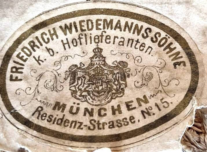 Klebeschild der Firma Friedrich Wiedemanns Söhne auf der Rückseite eines Portepees für einen bayerischen Kammerherrenschlüssel aus der Regierungszeit des Prinzregenten Luitpold von Bayern angebracht.